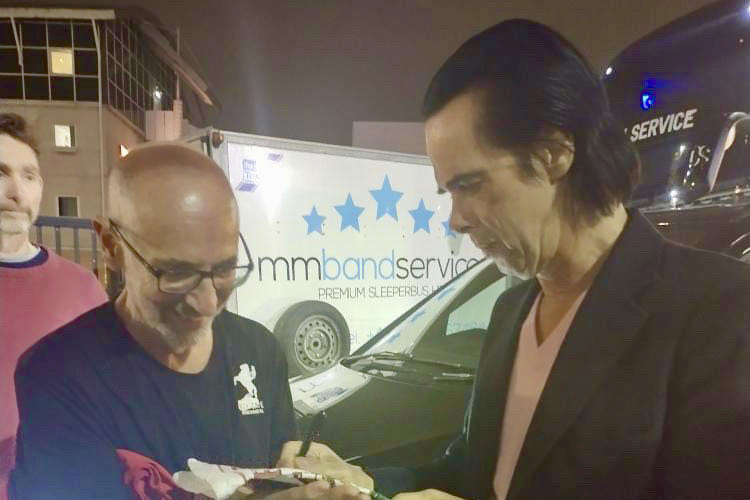 William McNicol holds the Warracknabeal tea towel as Nick Cave signs it.