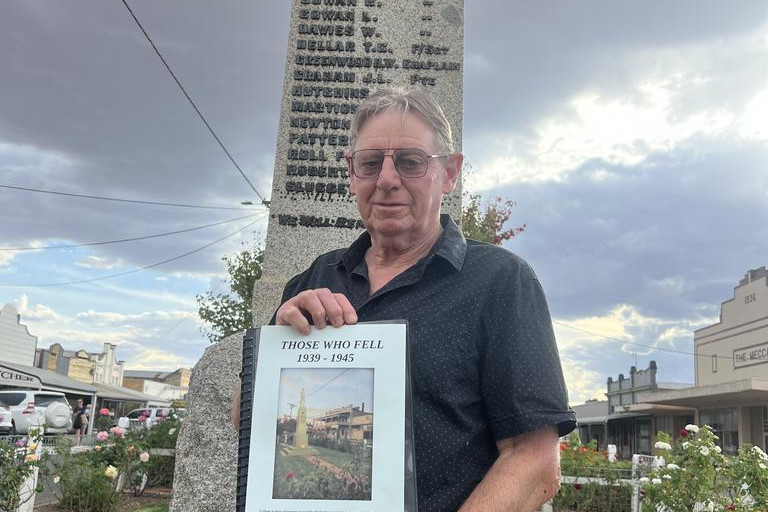 Friends of RSL Rainbow vice-president Don Pedder with a booklet 'Those Who Fell' in front of the Rainbow Cenotaph.
