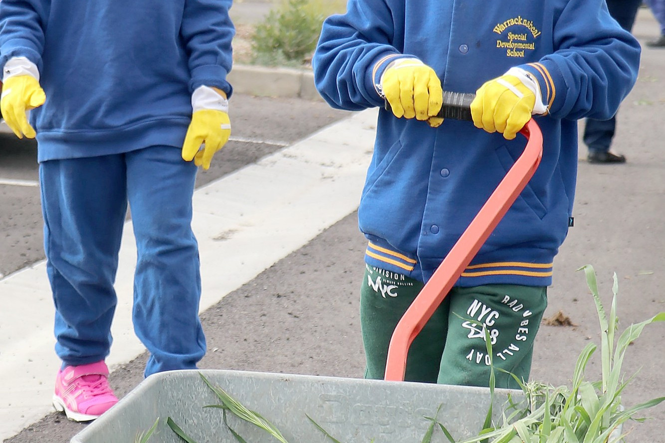 Lilly and Noah guide the wheelbarrow of weeds along the path.