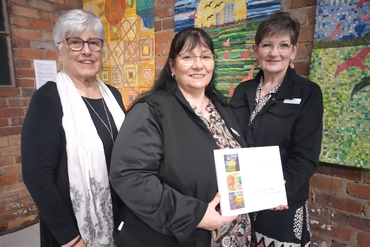 Project co-ordinator Nina Gould with Yarriambiack Mayor Kylie Zanker and Hopetoun Patchwork Group president Lynne Gould. The 'Growth' banners are in the background. Cr Zanker holds a book presented to the shire showing the development of the project.